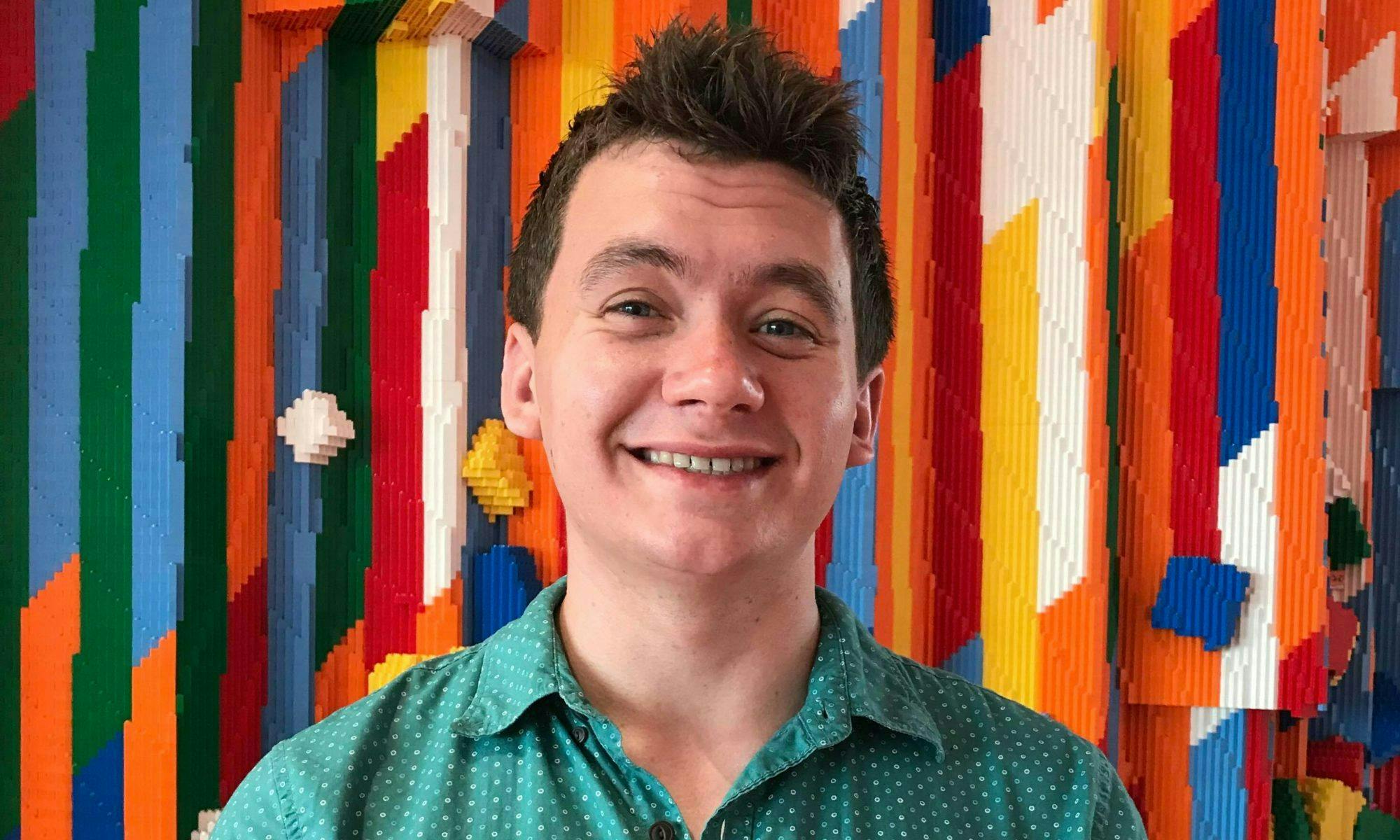 Sam Instone smiles to the camera in front of a bright colourful background